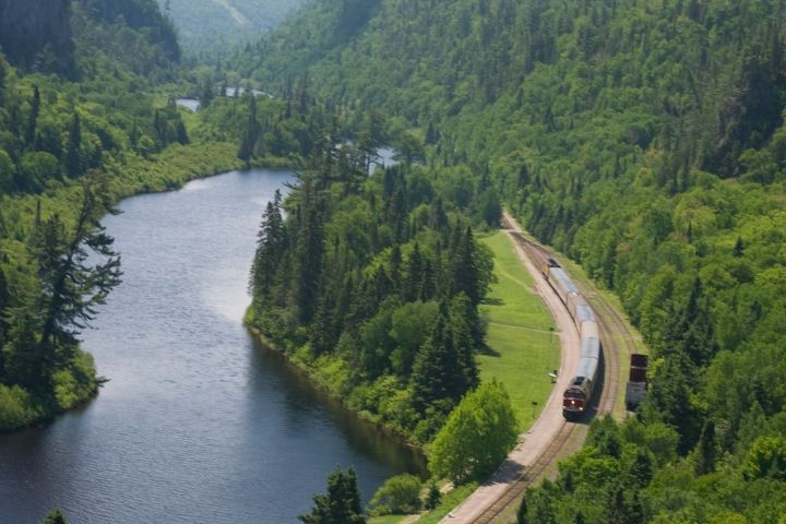 a train traveling down tracks next to a body of water surrounded by trees